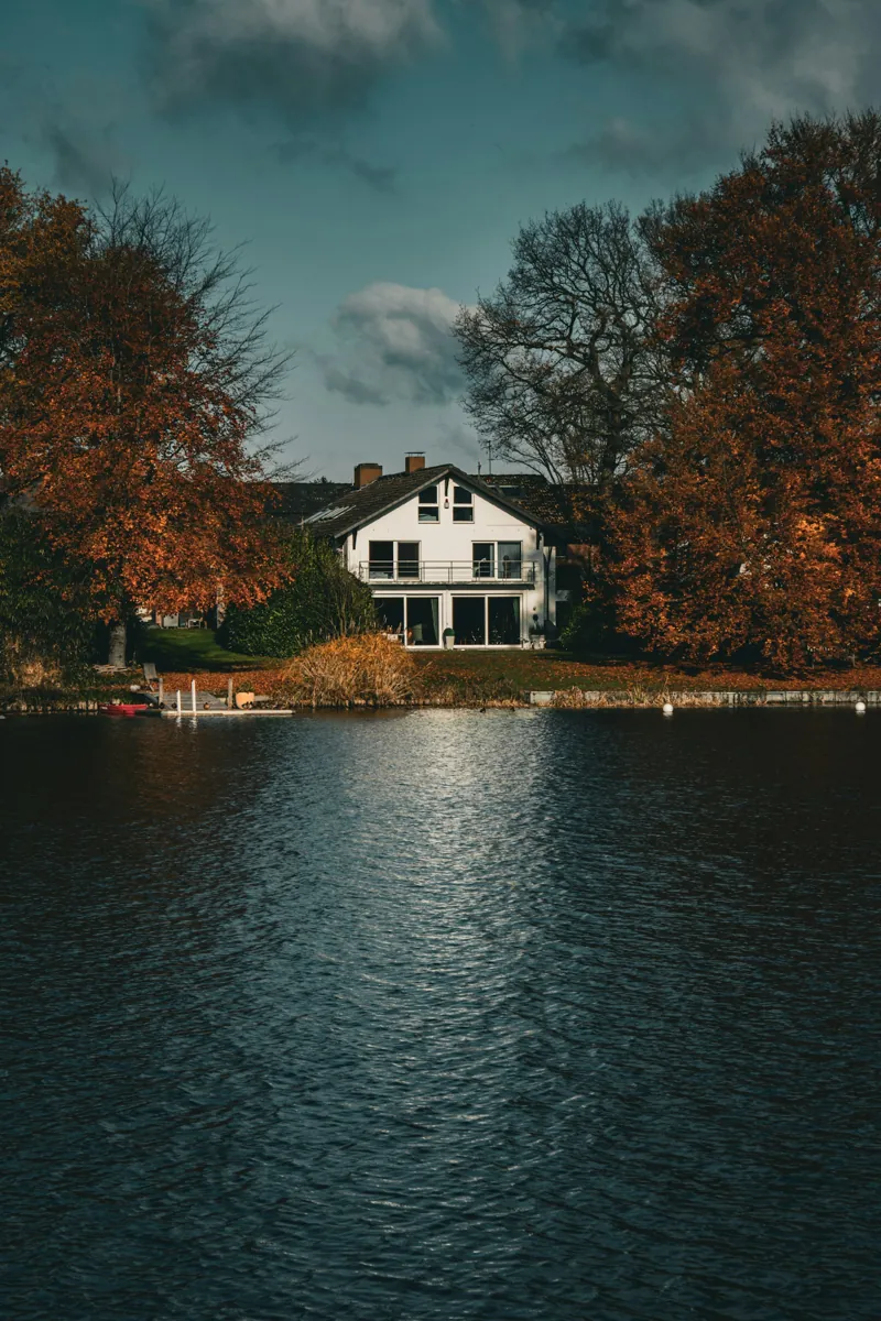 White lake house set back from the water among autumn trees