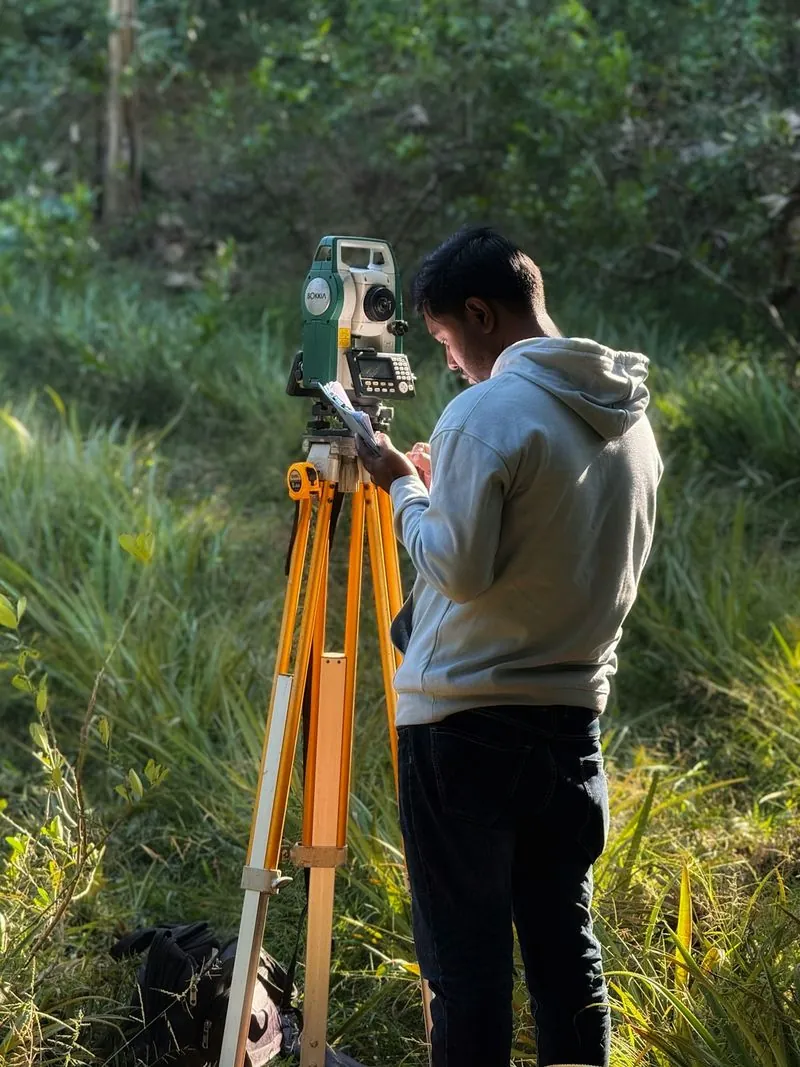 Surveyor using a total station in a grassy field