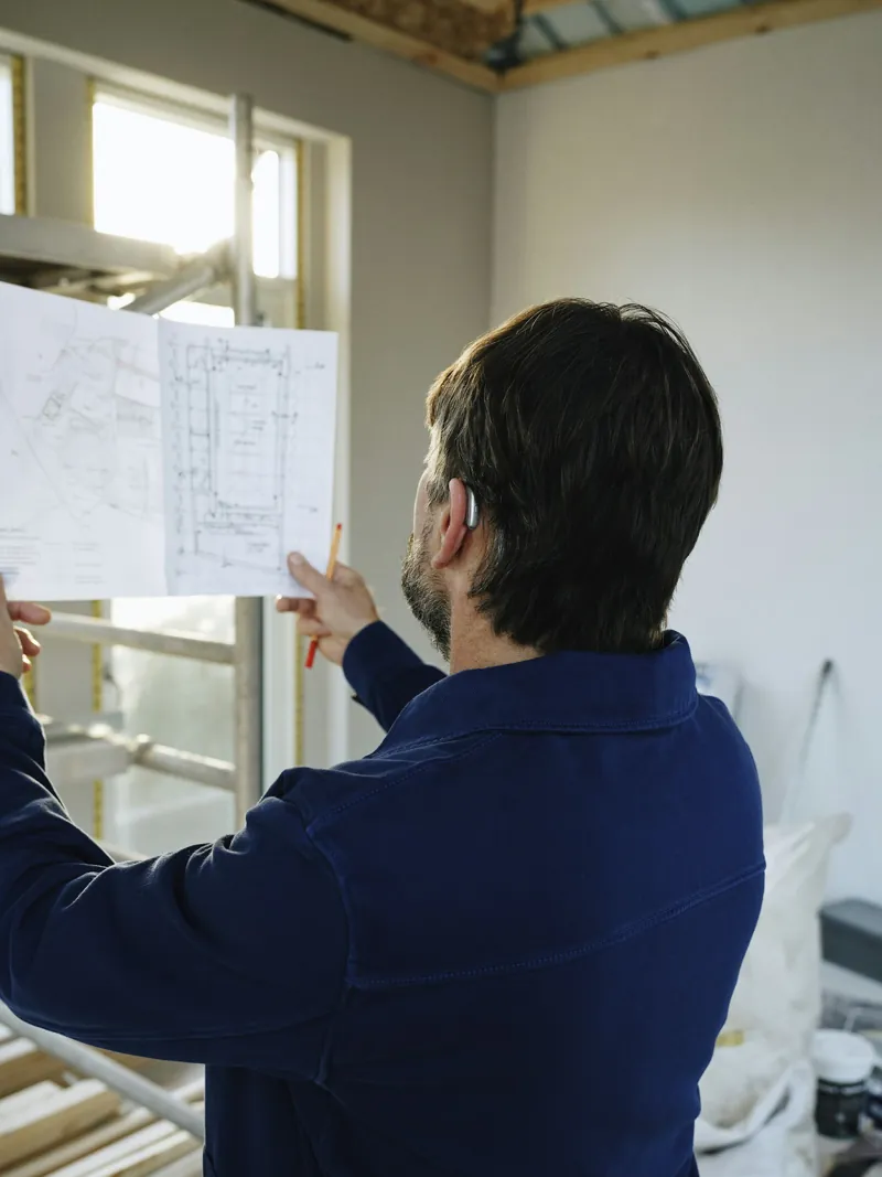 Man reviewing a floor plan drawing inside a house under construction